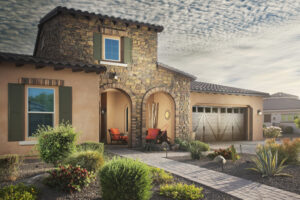 Desert landscaping with agave, shrubs, and grasses on gravel, with a stone pathway leading to a house entrance.