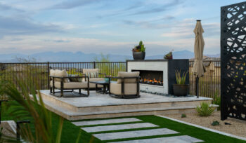Image of backyard: hardscaping, turf, travertine steps, trellis in the background and raised firepit on a sun deck.