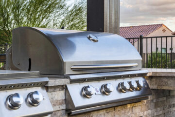 Close-up of built-in stainless BBQ grill set in a stone outdoor kitchen with warm sunset tones, designed by Kevens Landscape in Arizona.