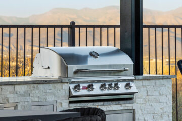 Built-in stainless BBQ grill and dining setup with white stone cabinetry overlooking desert mountains, designed by Kevens Landscape.