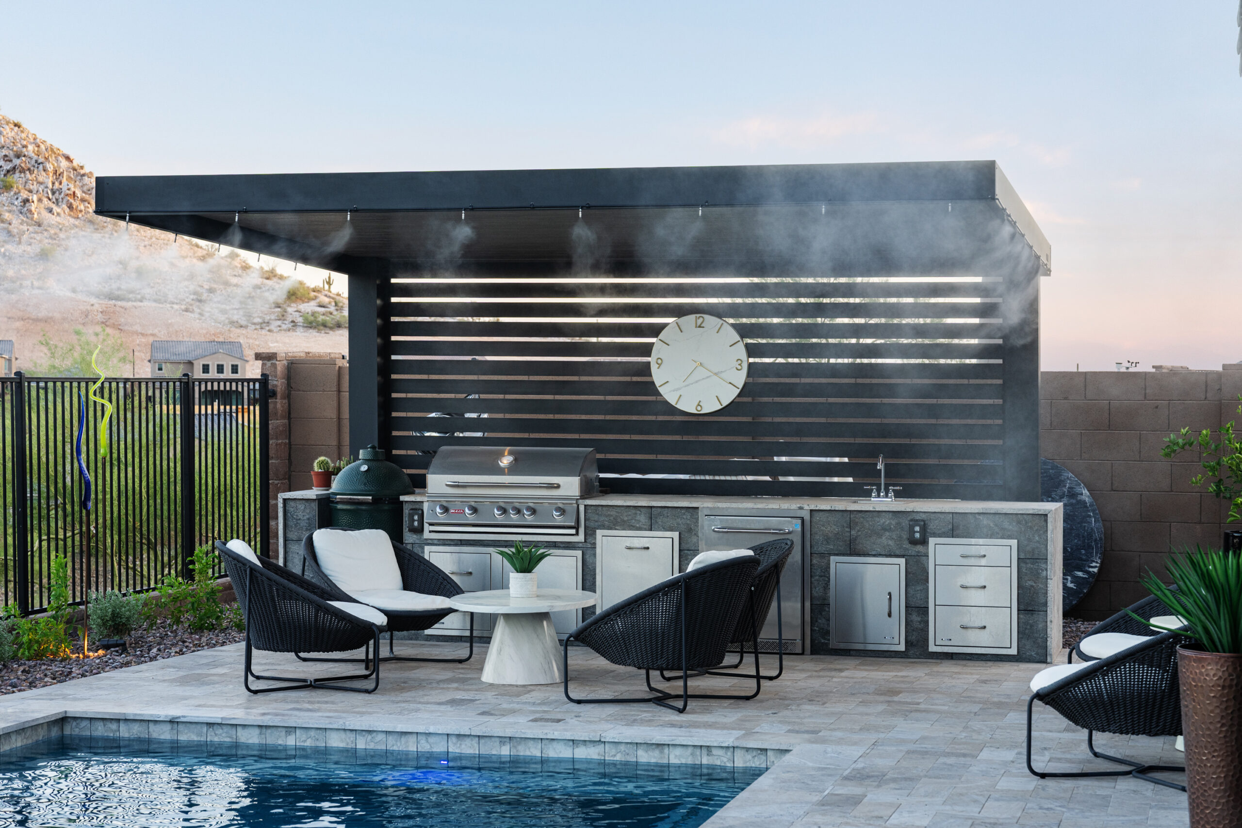 Modern Outdoor Kitchen with Pergola and Pool – Kevens Landscape AZ Alt text: Modern outdoor kitchen and BBQ area by Kevens Landscape featuring a stainless grill, pergola with misting system, and poolside seating in El Mirage, Arizona.